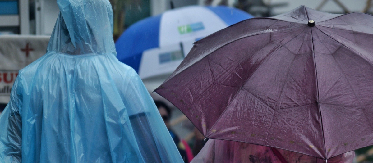 Dos personas con paraguas y chubasqueros pasen por la calle en un día de lluvias y tormentas
