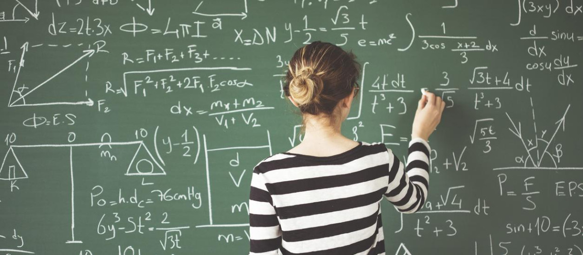 Young student writing with chalk on green chalk board in classroom