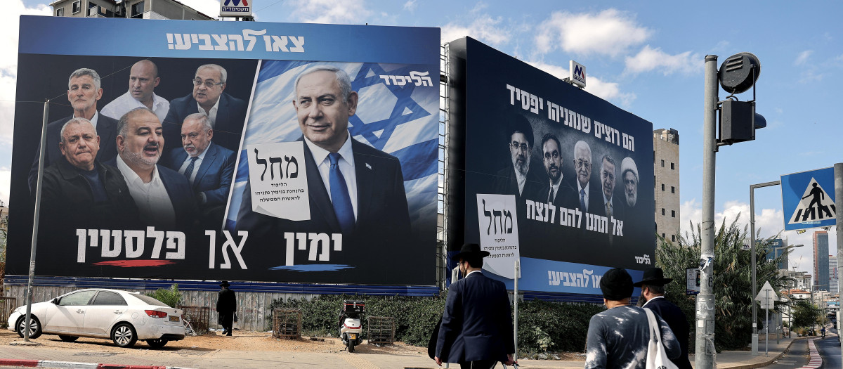 Los peatones cruzan una calle frente a una pancarta (izquierda) con la imagen del primer ministro israelí Benjamin Netanyahu, del partido Likud, y miembros de la oposición, antes de las elecciones legislativas del país en Bnei Brak