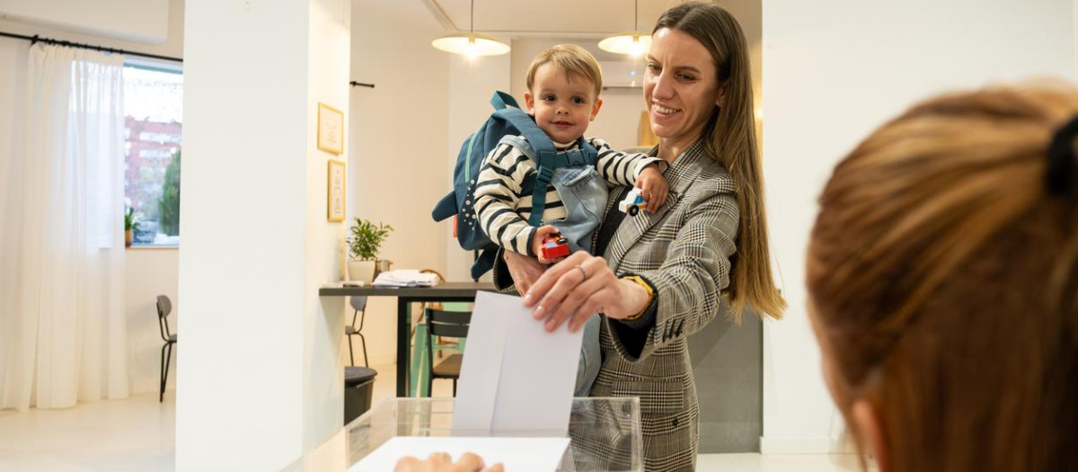 Una madre, junto a su bebé, introduce una papeleta en un colegio electoral