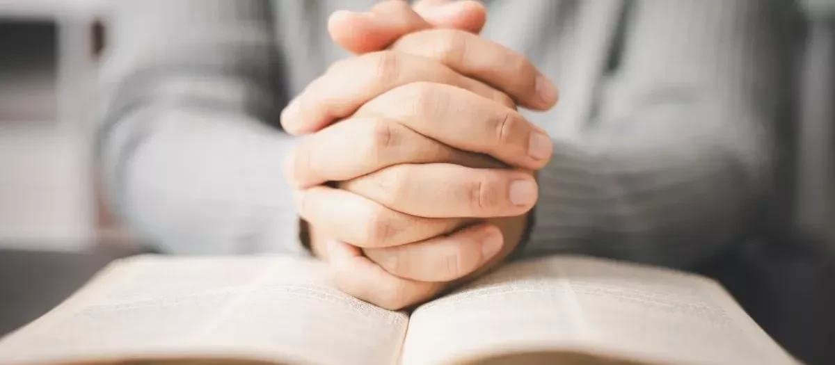 Una persona con las manos entrelazadas sobre una Biblia.