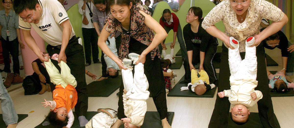 Chinese parents perform stretching exercises with their babies at a center in Xiamen, in southeast China's Fujian province, 01 April 2007, designed to improve the babies' alertness and balance. China's government has long viewed its population of 1.3 billion people, the world's largest, as the greatest challenge to the nation's modernisation, vowing to continue the nearly 30-year-old policy beyond 2033, when China's population is expected to peak at 1.5 billion people.     CHINA OUT GETTY OUT          AFP PHOTO (Photo by AFP / AFP)