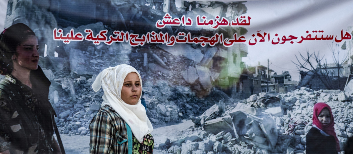 A woman walks past a banner showing a member of the Kurdish Women's Protection Units (YPJ) and reading in Arabic "we have defeated Daesh, will you now watch the Turkish assaults and slaughters against us?", during a protest and sit-in by Syrian Kurds against Turkey, in the town of Ras al-Ain in Syria's Hasakeh province near the Turkish border on August 9, 2019. (Photo by Delil SOULEIMAN / AFP)