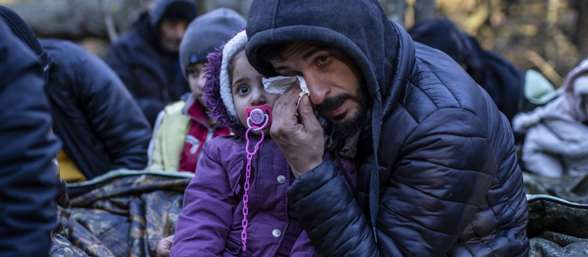 A man holding a child reacts as the members of the Kurdish family from Dohuk in Iraq wait for the border guard patrol, near Narewka, Poland, near the Polish-Belarus border on November 9, 2021. - The three-generation family of 16 members with seven minors, including the youngest who is five months old, spent about 20 days in the forest and was pushed back to Belarus eight times. They claim they were beaten and frightened with dogs by Belarusian soldiers. (Photo by Wojtek RADWANSKI / AFP)