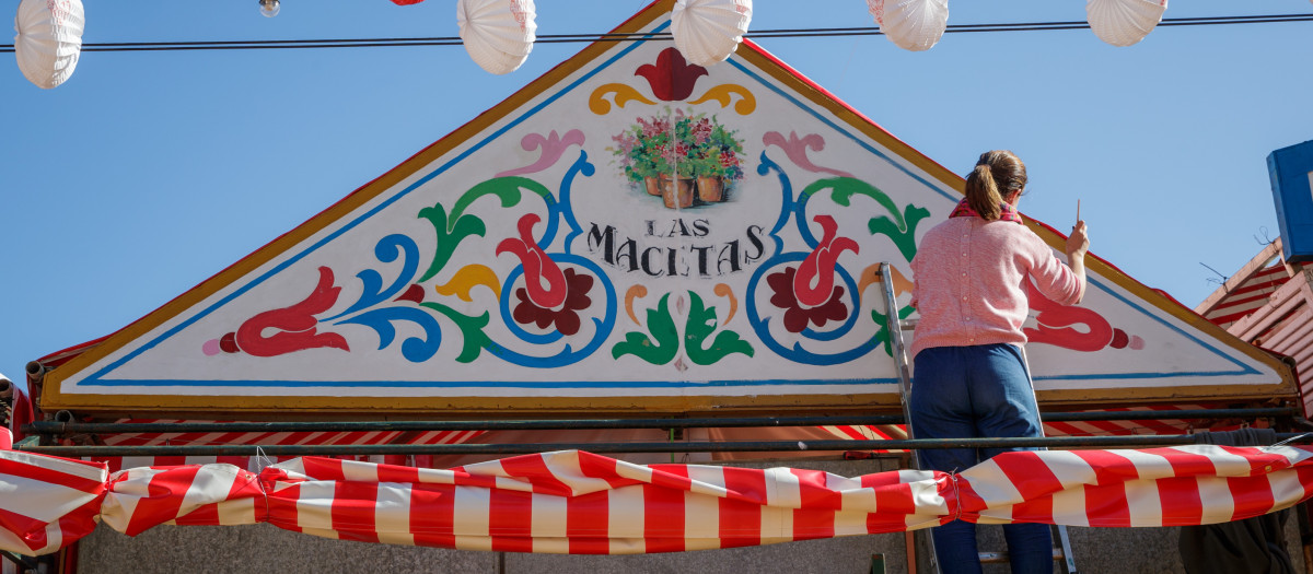 Una mujer repinta la fachada de una de las casetas del recinto ferial que se prepara para recuperar este fin de semana, tras dos años de pausa por la pandemia, su Feria de Abril, una fiesta en la que miles de personas se divierten en esta feria de Sevilla situada entre Los Remedios y Tablada, a las doce de la noche del sábado se encenderán 212.000 bombillas que alumbrarán sus 15 calles.