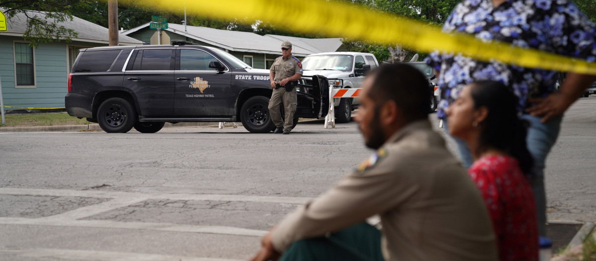 La gente se sienta en la acera afuera de la Escuela Primaria Robb mientras la policía estatal protege el área en Uvalde, Texas