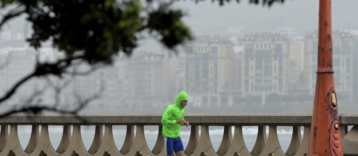 Un hombre, con chubasquero, corre por el Paseo Marítimo de La Coruña