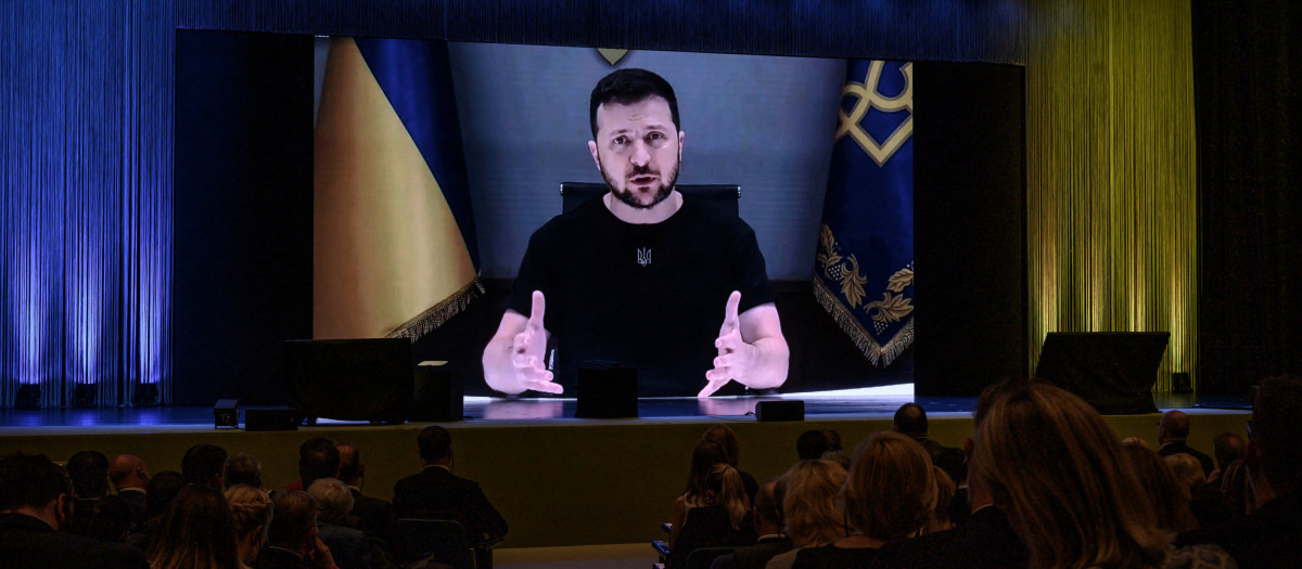 Ukraine's President Volodymyr Zelensky appears on a giant screen as he delivers a statement at the start of a two-day International conference on reconstruction of Ukraine, in Lugano on July 4, 2022. - Ministers from dozens of countries and organisations leadrers gathered in Switzerland Monday to hash out a "Marshall Plan" to rebuild the war-torn country. (Photo by Fabrice COFFRINI / AFP)