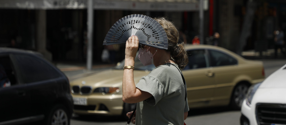 A woman crosses a street and covers herself with a fan in Palma de Mallorca during a heat wave.