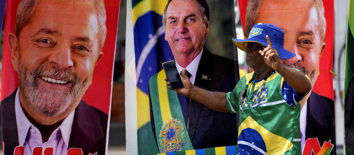 A demonstrator dressed in the colors of the Brazilian flag performs in front of a street vendor's towels for sale featuring Brazilian presidential candidates, current President Jair Bolsonaro, center, and former President Luiz Inacio Lula da Silva in Brasilia, Brazil, Tuesday, Sept. 27, 2022. Brazilians head to polls on Oct. 2 to elect a president, vice president, governors and senators. (AP Photo/Eraldo Peres)