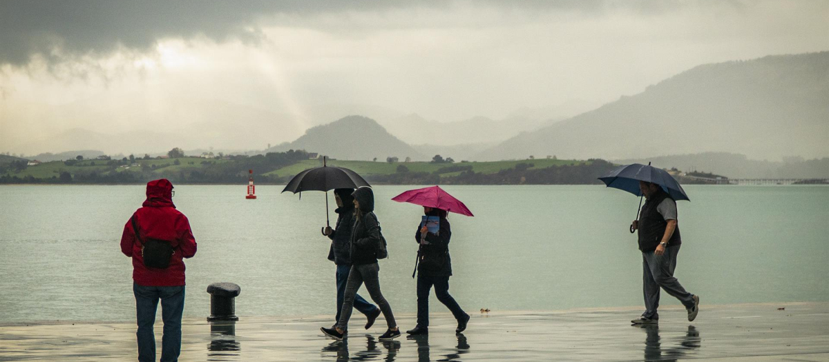 Gente pasea bajo la lluvia junto a la bahía de Santander