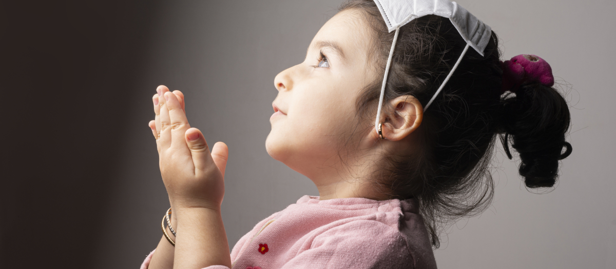 Praying Little girl wearing mask on her head in front of epidemic coronavirus outbreak, science vs religion coronavirus