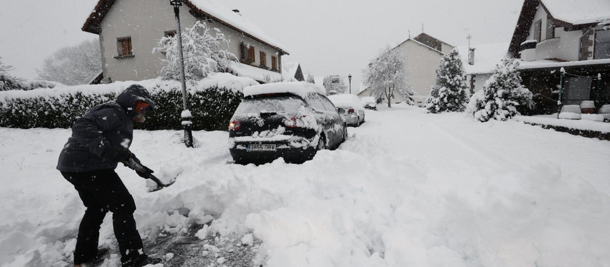 Una persona intenta limpiar de nieve para poder sacar su vehículo de una calle de la localidad de Espinal donde una intensa nevada caída durante la jornada de este lunes cubre completamente la carretera
