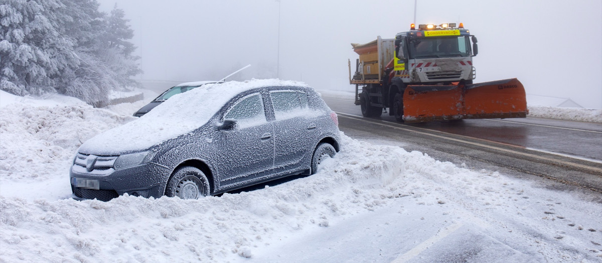 Un coche cubierto de nieve y una máquina quitanieves en Navacerrada