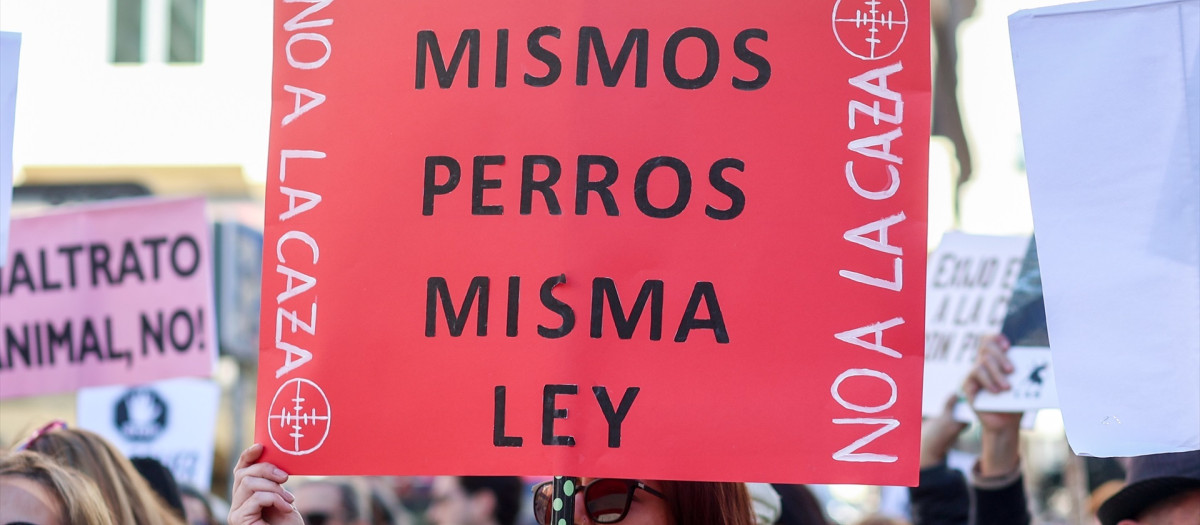 Una mujer sujeta una pancarta de 'Mismos perros misma ley' en una concentración bajo el lema ‘No a la caza’