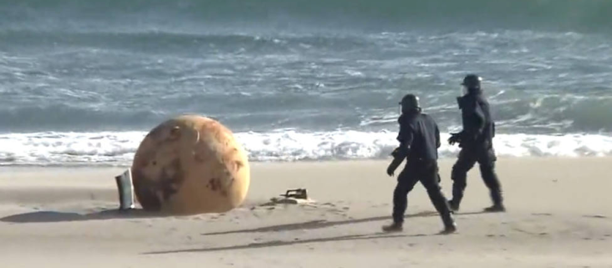 Dos agentes de Policía se aproximan a la enorme bola aparecida en una playa de Japón la semana pasada