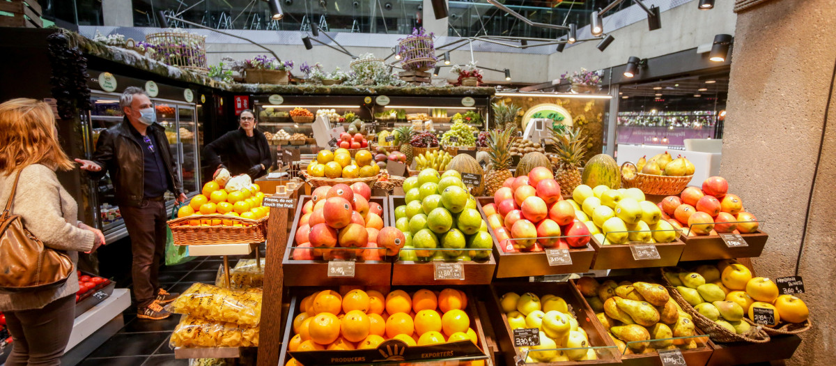 Varios clientes hacen la compra en un puesto de fruta en el mercado de San Antón en Madrid