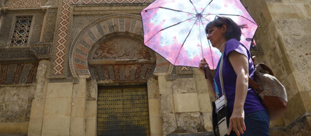 Una mujer se resguarda del sol con una sombrilla mientras camina junto a la Mezquita-Catedral de Córdoba