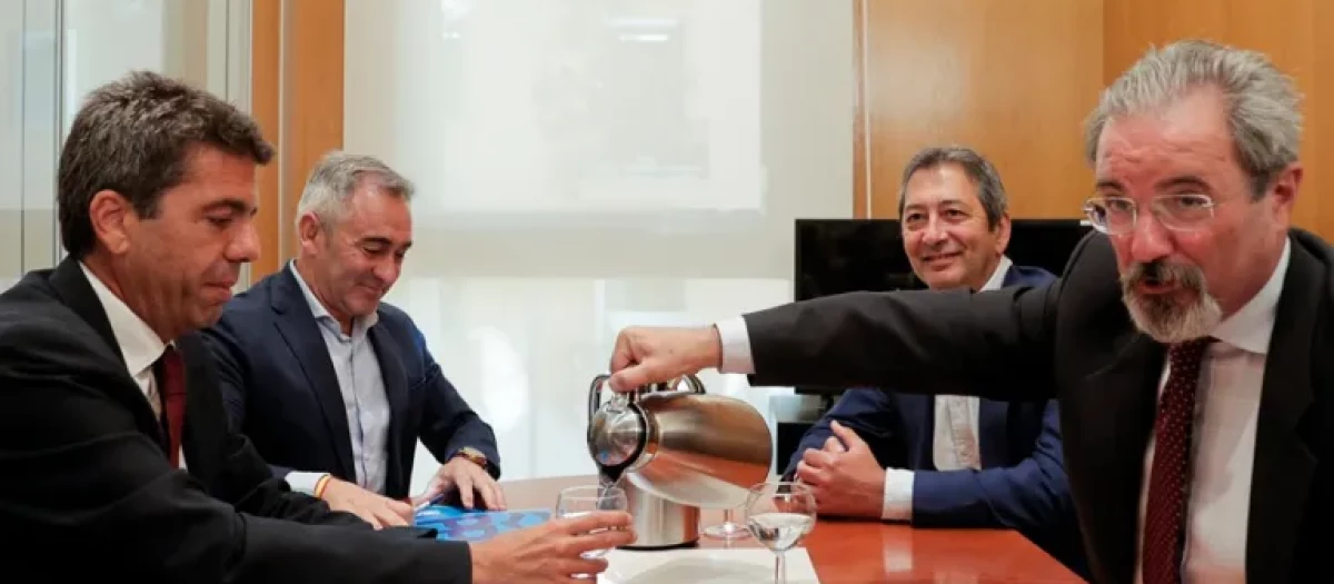 Carlos Flores, de Vox, sirve agua a Carlos Mazón en los momentos previos a la reunión con los populares.