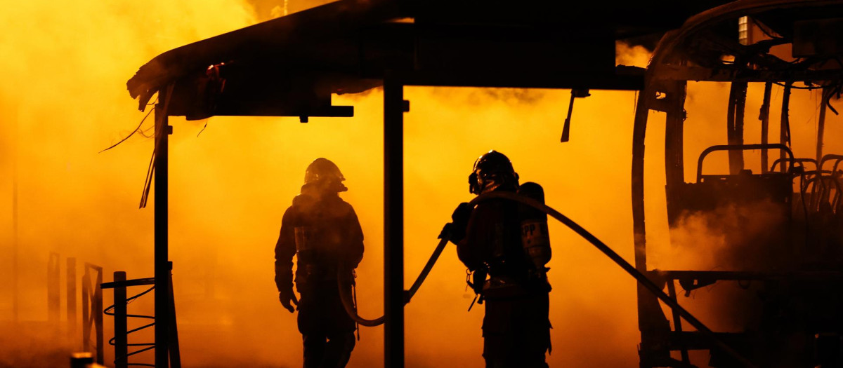 Los bomberos extinguen un autobús quemado durante los enfrentamientos entre los manifestantes y la policía antidisturbios