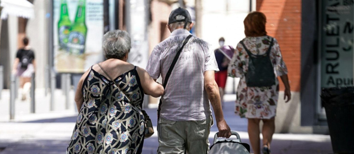 Una pareja de ancianos camina por la calle con un carro de compra.