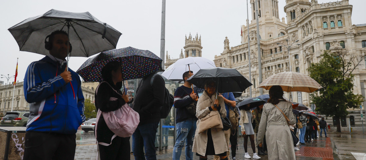 MADRID, 19/10/2023.- Varias personas se protegen de la lluvia con paraguas frente al Palacio de Cibeles, este jueves en Madrid. Cancelación de salidas de barcos, árboles caídos, inundaciones y problemas de alumbrado urbano son efectos de la borrasca Aline que mantiene en alerta a España por lluvia, viento y olas de hasta 10 metros, con un temporal que hará activar mañana el aviso rojo (por riesgo extremo) en las comunidades cantábricas. EFE/ Mariscal