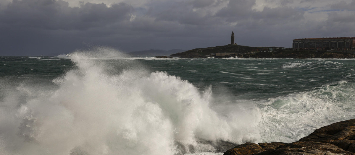 La Coruña sigue en alerta roja por la fuerza del viento y las olas. En la imagen una ola y al fondo la Torre de Hércules