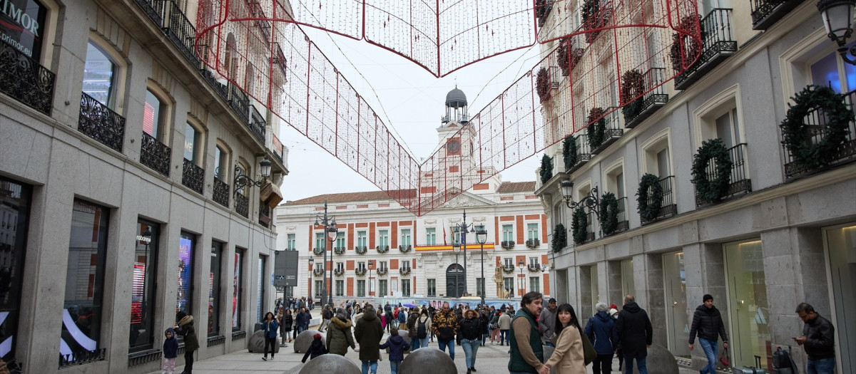 Varias personas en una calle comercial frente a la remodelada y peatonalizada Puerta del Sol