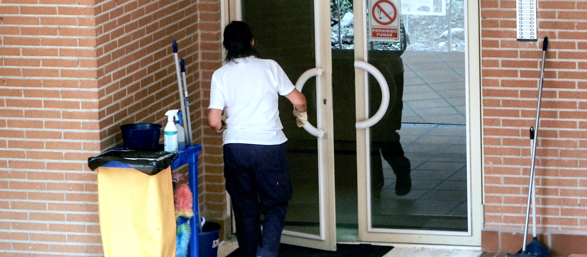 Una trabajadora de la limpieza entra en un edificio con el carrito de la limpieza