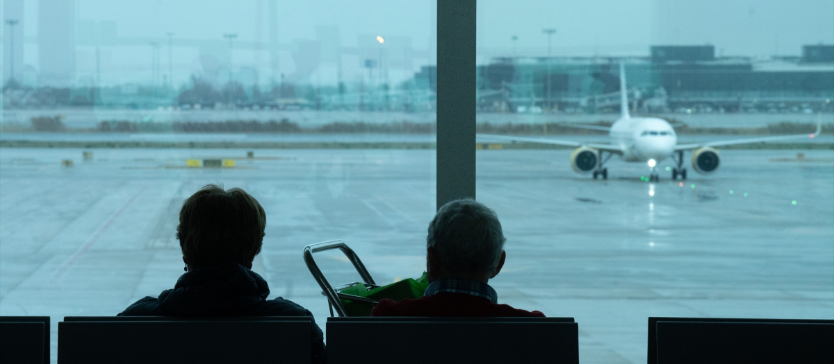 Dos personas esperan sentadas frente a un avión aparcado en la pista del aeropuerto de El Prat