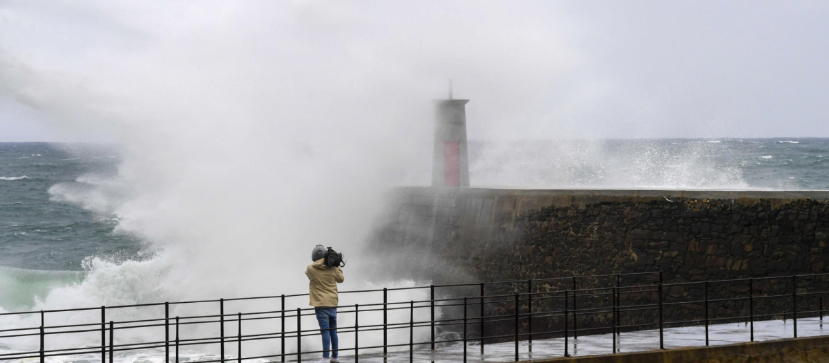 Un cámara toma imágenes de las grandes olas formadas por el temporal, en el puerto de Viavélez, Asturias