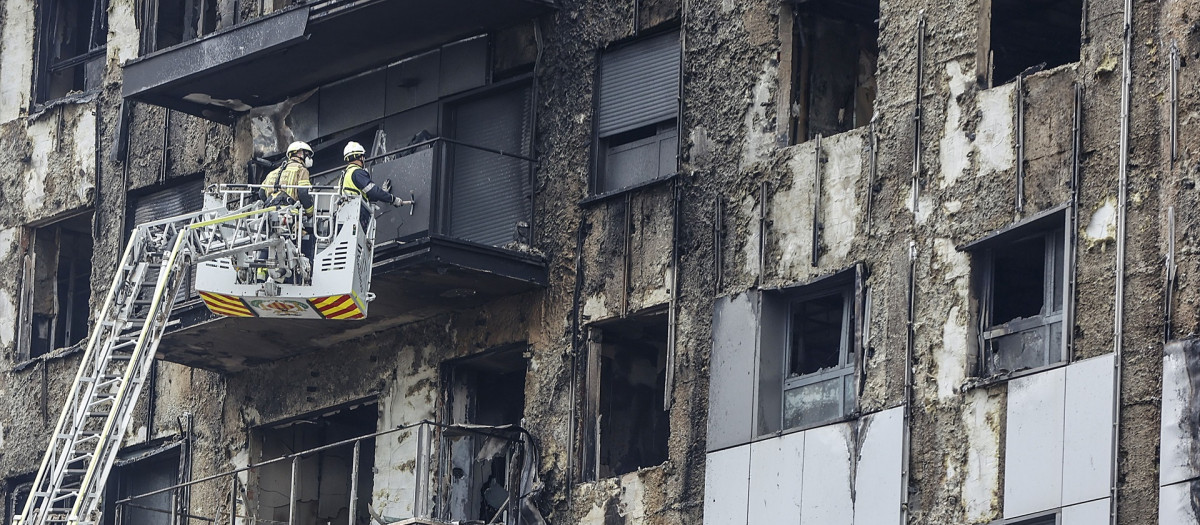 Bomberos en una grúa sanean la fachada del edificio incendiado, este lunes, en Valencia