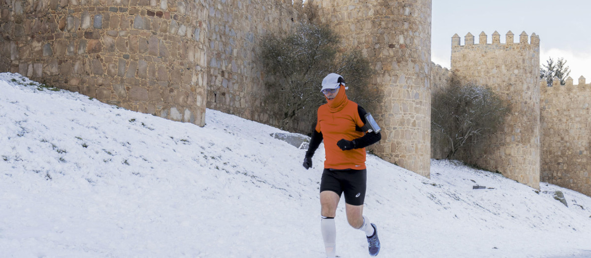 Un hombre corre en una calle cubierta de nieve frente a las murallas de Ávila