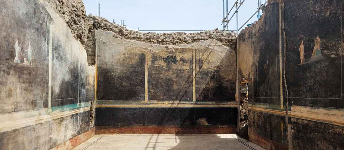 Un imponente salón de banquetes, de elegantes paredes negras y decorado con frescos con temas mitológicos inspirados en la guerra de Troya