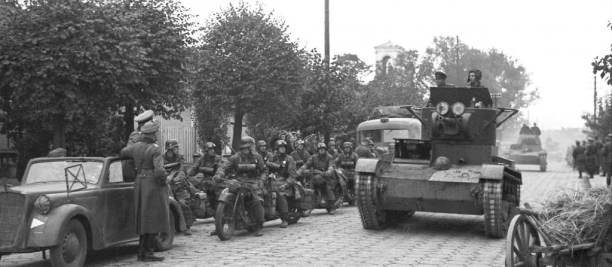 Tanque soviético T-26 desfilando frente a una columna motorizada alemana