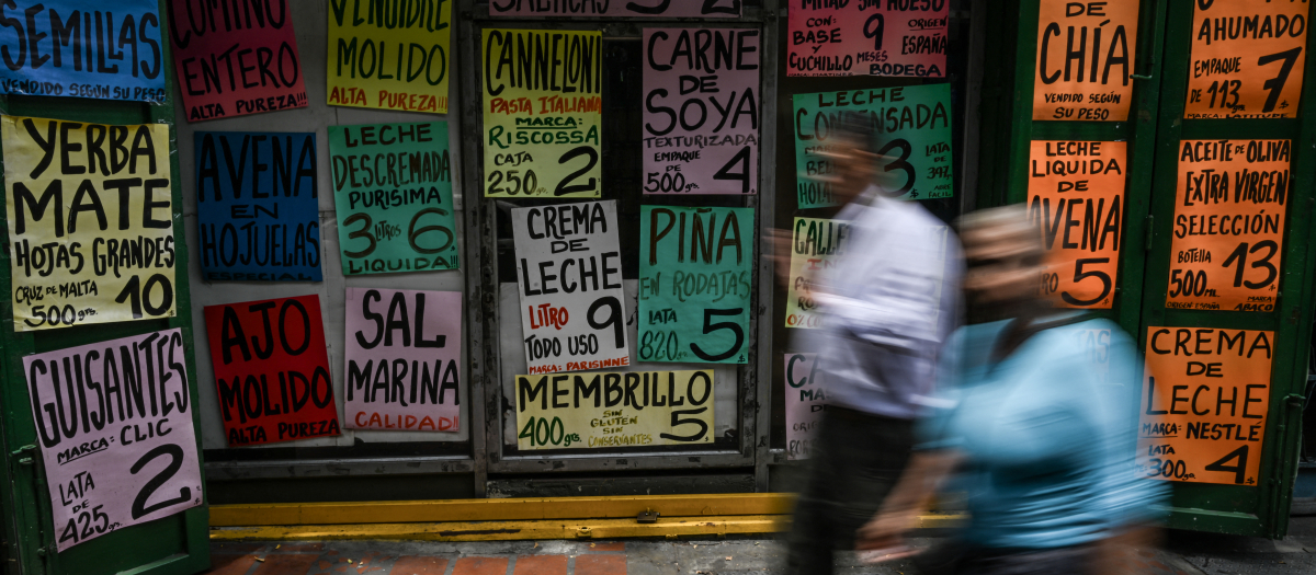 La gente pasa frente a la fachada de un supermercado que muestra los precios de los alimentos en Caracas