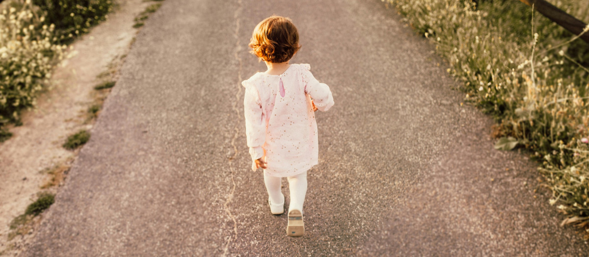 Niña vestida de blanco caminando por el asfalto