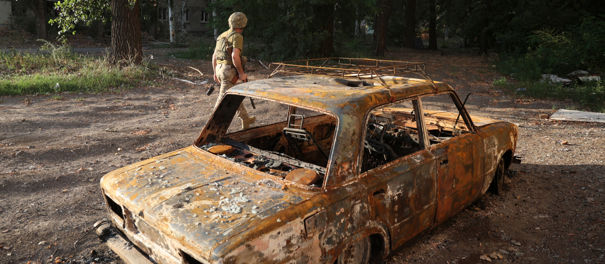 Un militar ucraniano pasa junto a los restos de un coche en la región de Donetsk