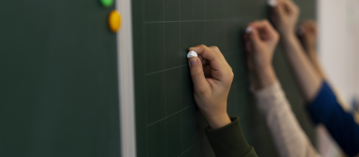 Imagen de varios alumnos escribiendo en la pizarra de un aula