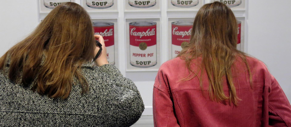 Dos mujeres fotografían las series de Andy Warhol sobre las latas de sopa Campbell