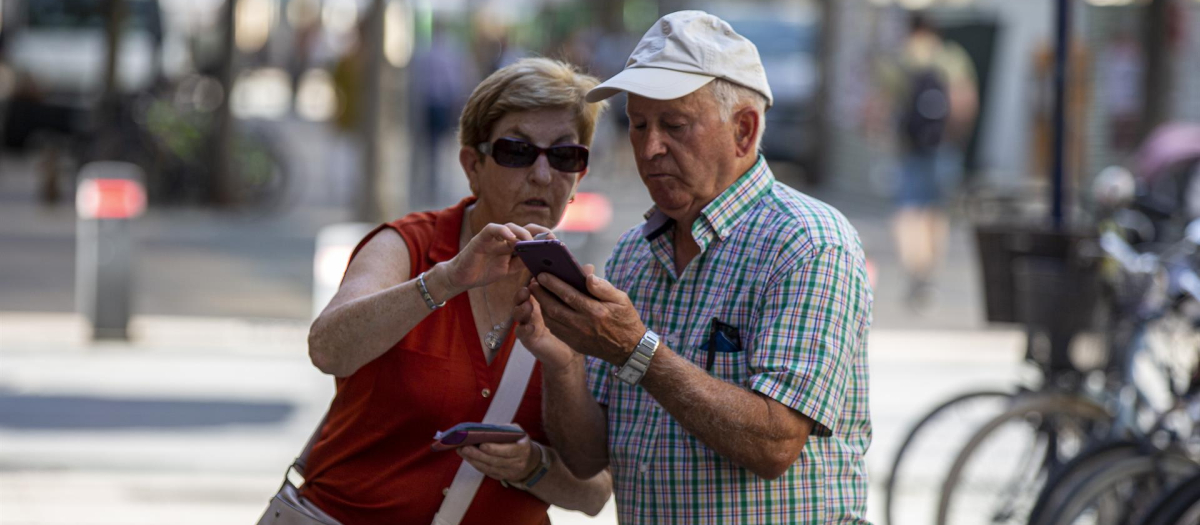 Dos personas mayores consultan un teléfono móvil