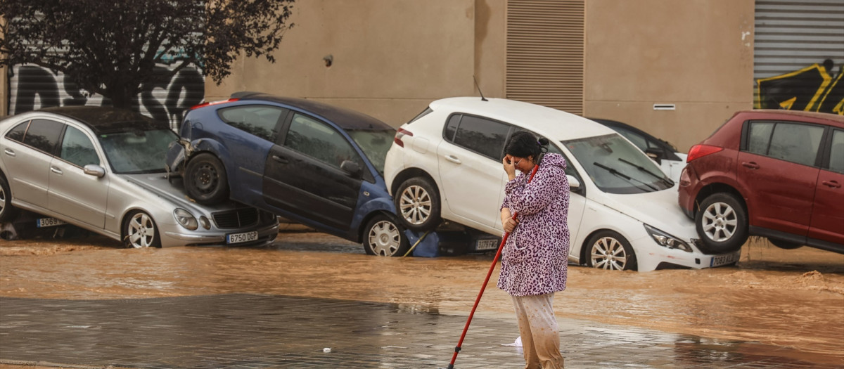 Una mujer realiza labores de limpieza junto a vehículos destrozados tras el paso de la DANA por el barrio de La Torre de Valencia