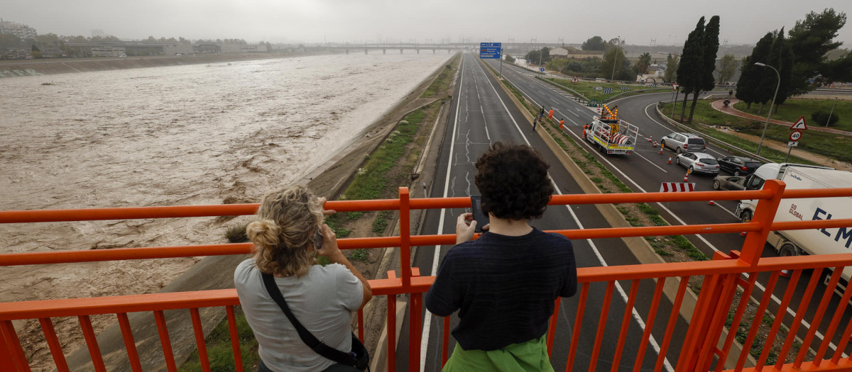 Dos personas contemplan el nuevo cauce del Turia repleto de agua a causa de la gota fría