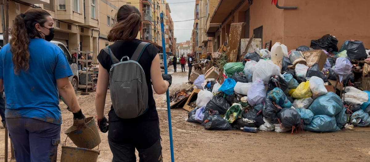 Dos chicas voluntarias pasan al lado de una montaña de basura