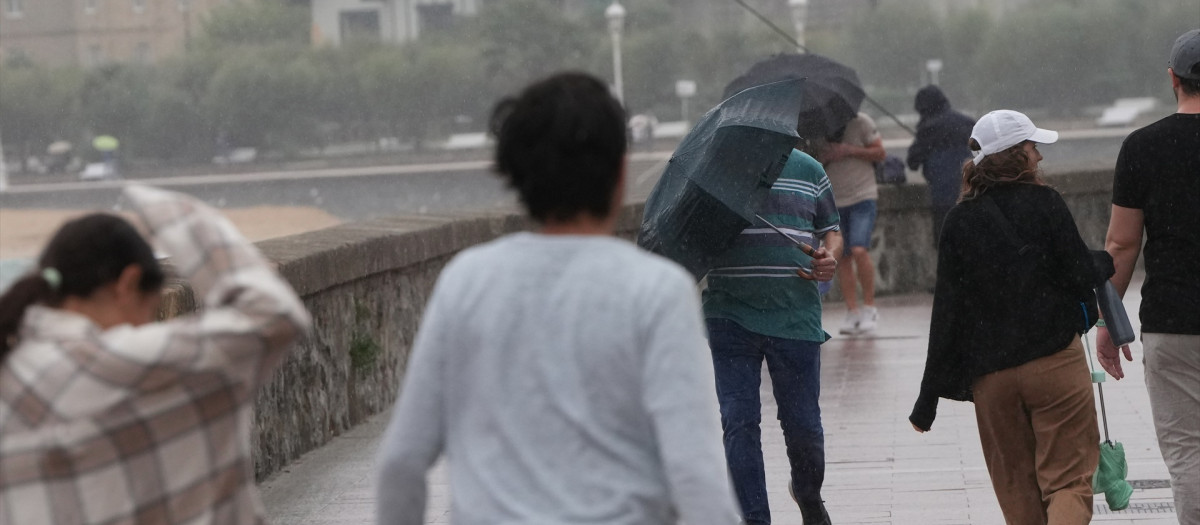 Varias personas caminan bajo la lluvia en la playa de Ondarreta, en San Sebastián