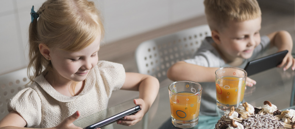 Niños comiendo con el móvil en la mano