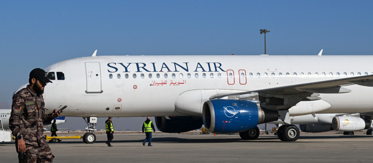 Un combatiente pasa caminando mientras el personal de tierra prepara un avión de Syrian Air para despegar hacia la ciudad de Alepo, en el aeropuerto internacional de Damasco