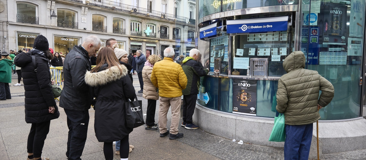 Varias personas hacen cola para comprar lotería para el Sorteo Extraordinario del Niño en la administración de lotería 'El Doblón de Oro'