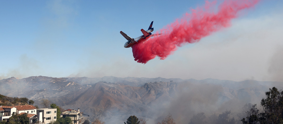 Un avión de extinción de incendios arroja el retardante de fuego Phos-Chek cerca de las casas durante el incendio de Palisades