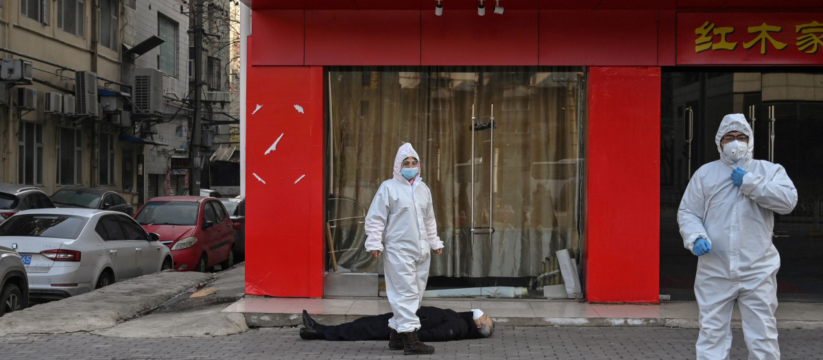 Esta foto tomada el 30 de enero de 2020 muestra a funcionarios con trajes protectores que revisan a un anciano que llevaba una mascarilla y que se desplomó y murió en una calle cerca de un hospital en Wuhan